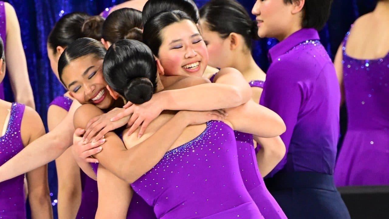 Skaters in purple dresses hugging and smiling after a performance