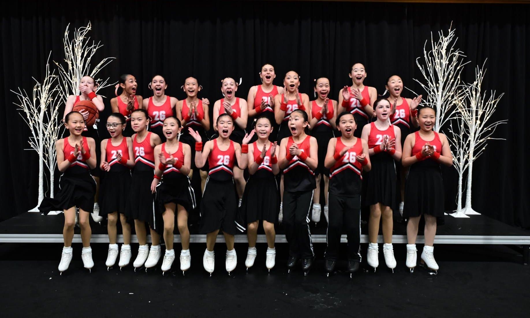 A team of young skaters in red and black, clapping and cheering together on a stage