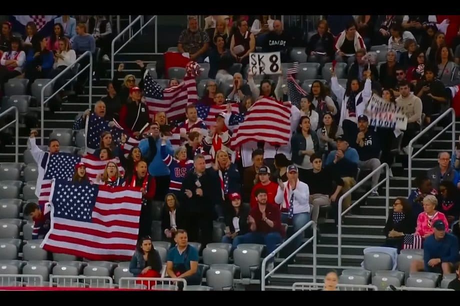 A full crowd in the stands at a championship, supporters waving United States flags